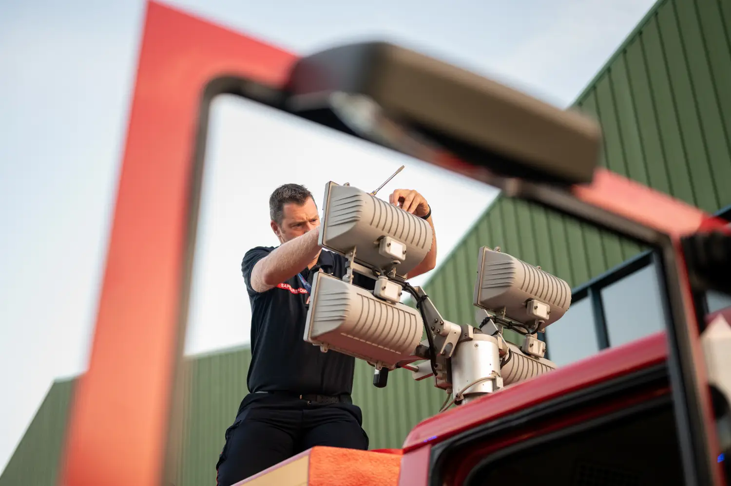 Un sapeur-pompier ajuste des projecteurs d'éclairage sur le toit d'un camion rouge, par Vincent Delesvaux, photographe et vidéaste à Lyon.