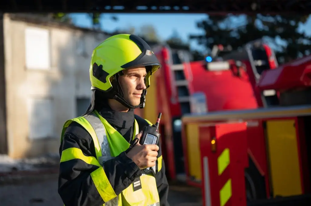 Un jeune sapeur-pompier au casque jaune communique avec un talkie-walkie devant son camion, par Vincent Delesvaux, photographe et vidéaste à Lyon.