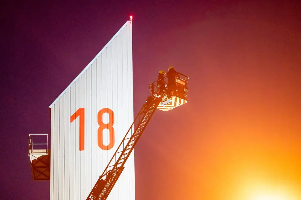 Composition graphique nocturne de la nacelle d'un camion de pompier près de la tour portant le numéro 18, par Vincent Delesvaux, photographe et vidéaste à Lyon.